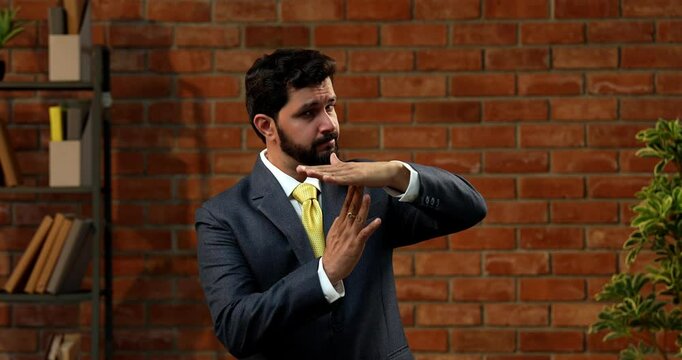 Indian businessman making take-a-break hand gesture in stylish office, Asian CEO or entrepreneur with beard suggesting pause or timeout while wearing formal suit and tie in office