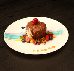 Elegant chocolate dessert covered with rich chocolate coating, decorated with fresh berries, mint leaves, and colorful artistic sauce strokes, beautifully plated on a white dish, ideal for fine dining