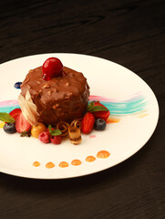 Elegant chocolate dessert covered with rich chocolate coating, decorated with fresh berries, mint leaves, and colorful artistic sauce strokes, beautifully plated on a white dish, ideal for fine dining