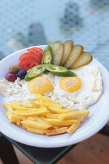Plate with sunny side up eggs, French fries, sliced pickles, tomatoes, and cucumbers, placed on a glass table, light breakfast or brunch scene with fresh ingredients, nutritious and colorful