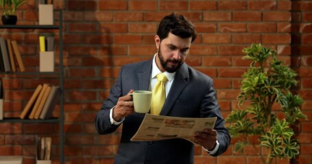 Indian businessman reading newspaper with coffee in cozy office. Asian CEO or entrepreneur in formal suit with beard stands against brick wall catching up on daily business news - Powered by Adobe