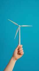 Hand Holding a Small Wind Turbine Model Against a Blue Background Representing Renewable Energy and Sustainability