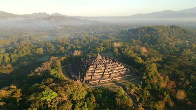 Aerial view of ancient Borobudur temple, surrounded by tropical misty jungle and soft morning light in Central Java, Indonesia.