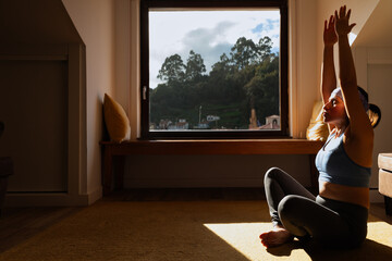 Woman doing yoga in the morning by her bright window.