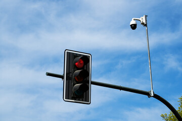 Stop signal: red traffic light illuminated on pole with CCTV security camera monitoring intersection. Urban transport regulation and smart city surveillance concept