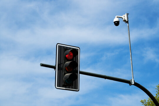 Stop signal: red traffic light illuminated on pole with CCTV security camera monitoring intersection. Urban transport regulation and smart city surveillance concept