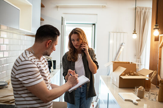 Couple unpacking boxes in their new kitchen while woman talks on the phone