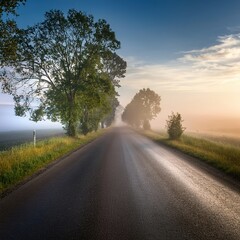 Fototapeta premium Scenic misty road at sunrise with lush greenery and clear sky