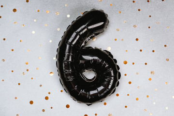 Black balloon number six on a sparkly gold dotted background for celebration