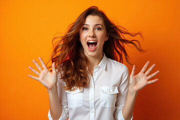 A woman with long brown hair, wearing a white shirt, looking surprised with her hands raised, against an orange background.