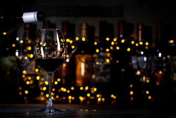 Red wine pours into glass and bottles on black bar background with lights