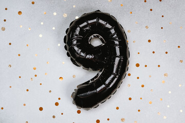 Black number nine balloon on a festive backdrop with golden confetti