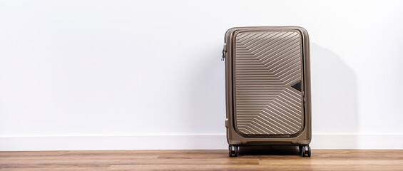 Elegant beige plastic suitcase on wheels in room with white wall, ready for trip or travel