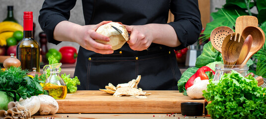 Chef assistant peels organic root celery.. Cozy kitchen with wooden table, kitchenware, vegetables, herbs and ingredients for cooking. Healthy vegan food, culinary, recipes, blogging