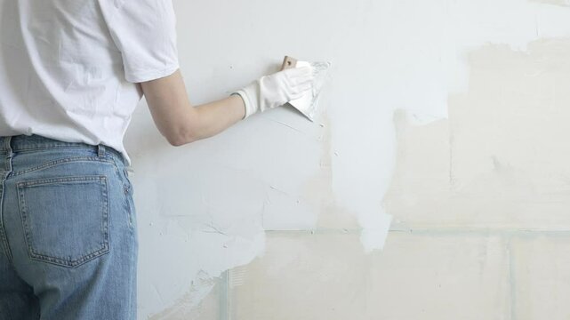 Unknown female construction worker applying plaster with putty knife, smoothing wall surface during home renovation, fixing wall imperfections with professional drywall repair technique, close up