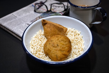 Puffed rice in a bamboo basket with Samosa, a crispy and spicy Indian triangle shape snack with tea, spectacles and newspaper in the morning, creating a warm and nostalgic ambiance