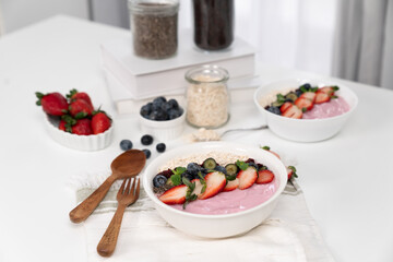 Presented by fruits putting yogurt toppings with strawberry, berry, oats, raisins and chia seed decorated by peppermint in white blow. Pink background. Set of healthy dairy product choice. Pecuniary.