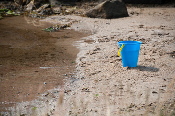 Blue plastic bucket on sandy beach by water. © Trygve