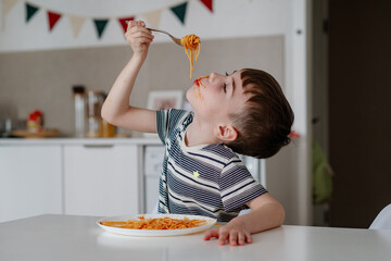 A charming boy eats spaghetti with tomato bolognese. A happy child eats freshly prepared healthy food indoors