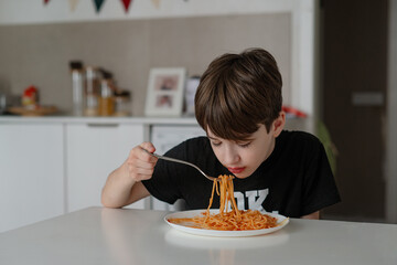 A teenage boy eats spaghetti with tomato bolognese. Child eats freshly prepared healthy food indoors