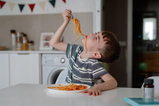 A charming boy eats spaghetti with tomato bolognese. A happy child eats freshly prepared healthy food indoors - Powered by Adobe