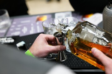 Skillful bartender pours whiskey into a jigger at a trendy cocktail bar