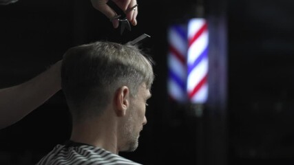 Professional barber grooming male client's hair with scissors, vintage barber pole framing traditional barbershop background