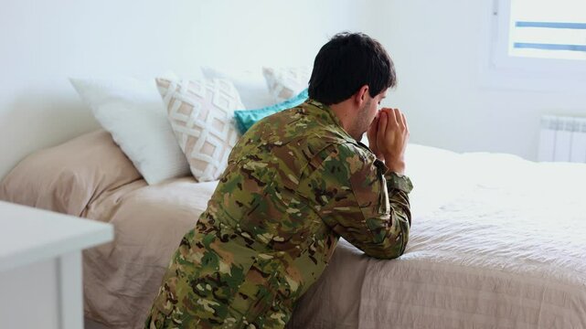 Depressed soldier kneeling and praying by his bed