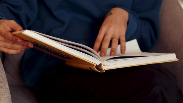 Amsterdam, Netherlands &ndash; 10april , 2025, 1987cinema book,a man seated in a comfortable armchair flipping through the pages of a hardcover book. The image captures his hands gently turning 