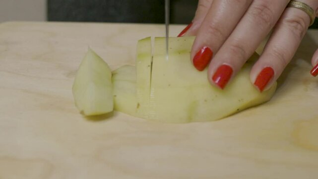 Close-up of hands slicing a peeled potato into cubes on a wooden chopping board, representing kitchen preparation process and culinary techniques in home cooking and food styling settings.