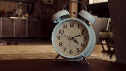A time-lapse video captures the rapid motion of clock hands on a vintage white alarm clock placed on a wooden table in a warmly lit room. The accelerated passage of time highlights the relentless