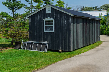 Viewed from the side a black wooden shed with white framed window, and pliable metal table on the lawn