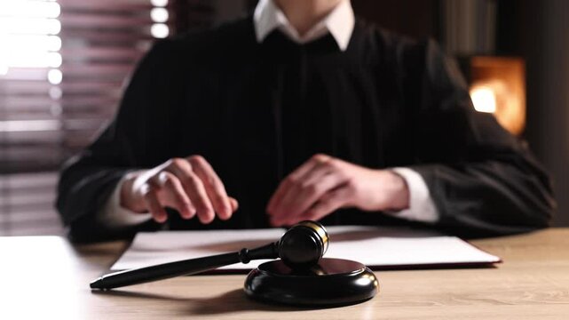 Judge hitting gavel and closing folder with judgement at wooden desk indoors, closeup