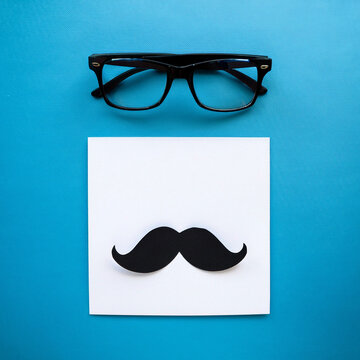 Feliz D&iacute;a del Padre, composici&oacute;n con bigote negro y gafas sobre fondo azul, tarjeta de felicitaci&oacute;n con hoja de papel blanca y lugar para texto