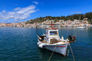 Traditional fishing boat floating in the blue sea near the colorful coastal town of Poros, Greece, under a bright sky.
