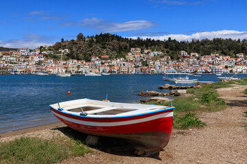 Traditional fishing boats on the shore facing the charming town of Poros, Greece, with calm sea and blue skies.