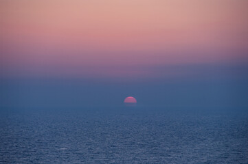 A beautiful sunset over the ocean with a large sun in the sky