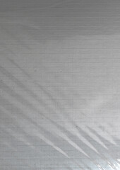 Obraz premium Minimal abstract texture featuring a soft light reflection across a slightly transparent, grid-patterned foil overlaying paper.