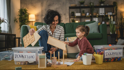 Mother and toddler daughter at home choose toys for charity donation