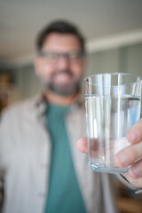 Man holding glass of water in focus, promoting health and hydration