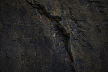 A natural stone texture background with chiaroscuro lighting, featuring a monolithic rock formation. Cracks and fragments emphasize its geological strength, ideal for design templates or science
