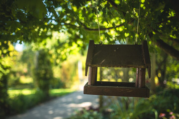 A wooden bird feeder suspended from a leafy tree in a peaceful outdoor setting.