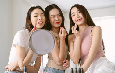 Three beautiful youn Asian women doing makeup and testing lipsticks on together in living room....