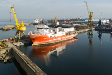 Industrial maritime scene: A large ship undergoing repair or loading at a dock in a busy port with...