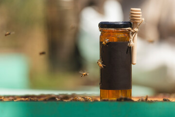 Jar of honey with black label and dipper surrounded by bees on beehive frame
