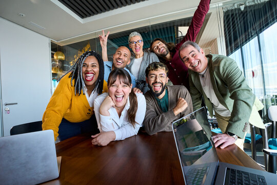 Multicultural coworkers laughing during a lively office meeting, showcasing teamwork, friendship, success, and a vibrant corporate atmosphere.