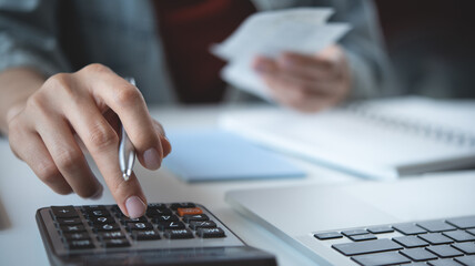 Close up woman hand using calculator to calculate home finance, accounting with laptop computer on...