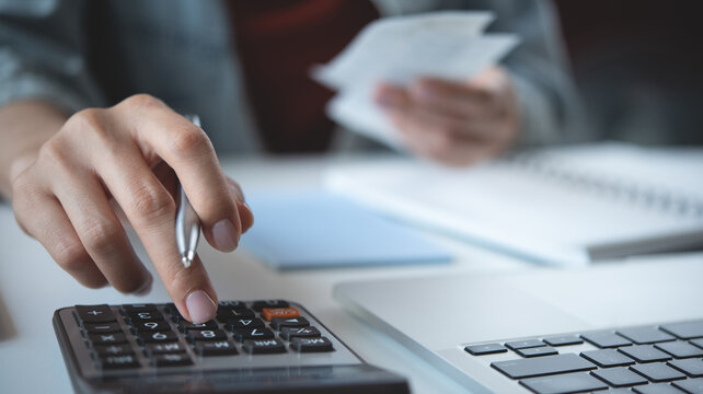 Close up woman hand using calculator to calculate home finance, accounting with laptop computer on table, budget management, monthly expenses. Doing finance, budgeting and tax calculation