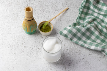 Matcha tea preparation with milk foam, whisk and powder on light background
