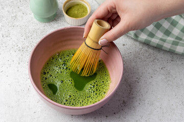 Woman whisking matcha tea in pink bowl with bamboo whisk